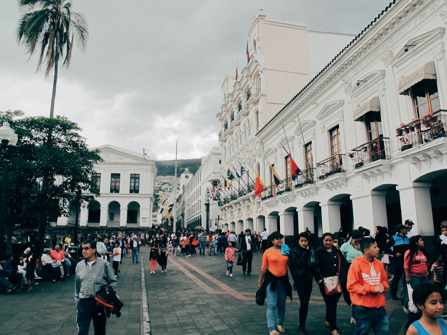 Crowds walk along a historic street lined with colonial buildings.