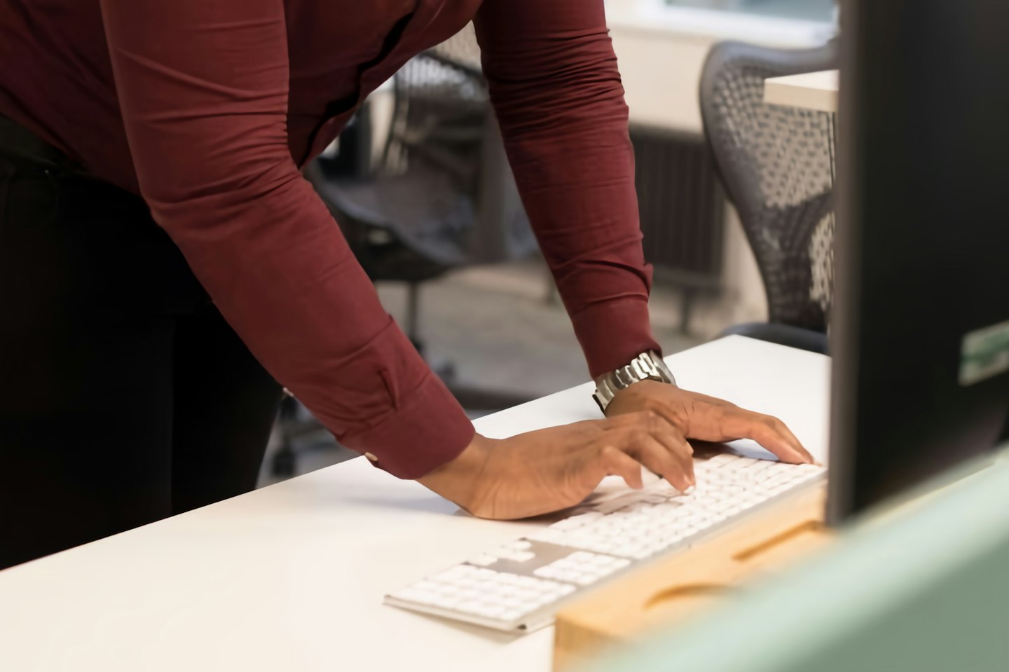 Hands wearing a silver watch typing on a white keyboard.